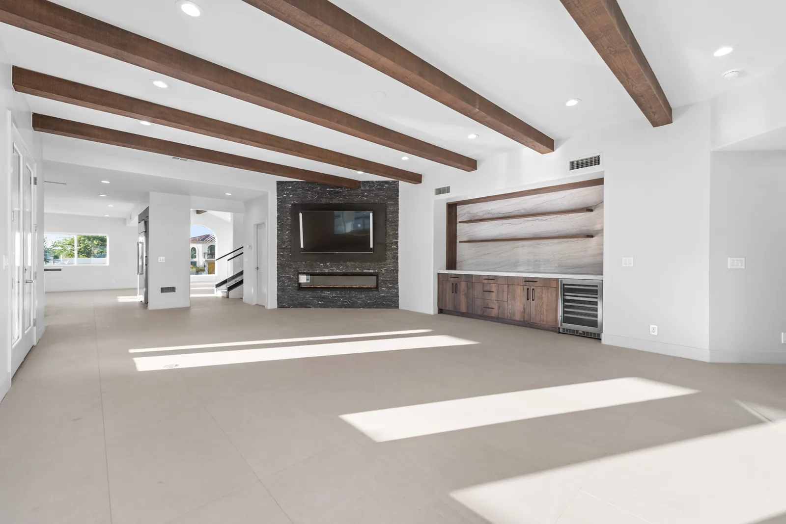 Beamed Great Room: Exposed timber beams over a linear fireplace and built-in millwork, with a wall of glass to the patio.
