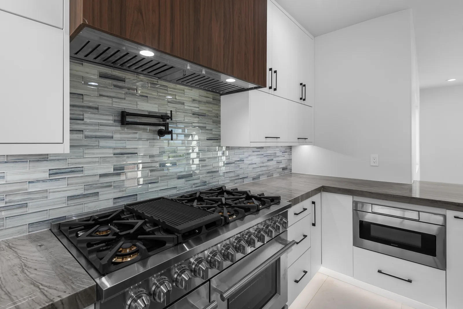Chef's Range Wall: Professional range with a custom hood surround and linear glass mosaic. Tile set by our own flooring crew.