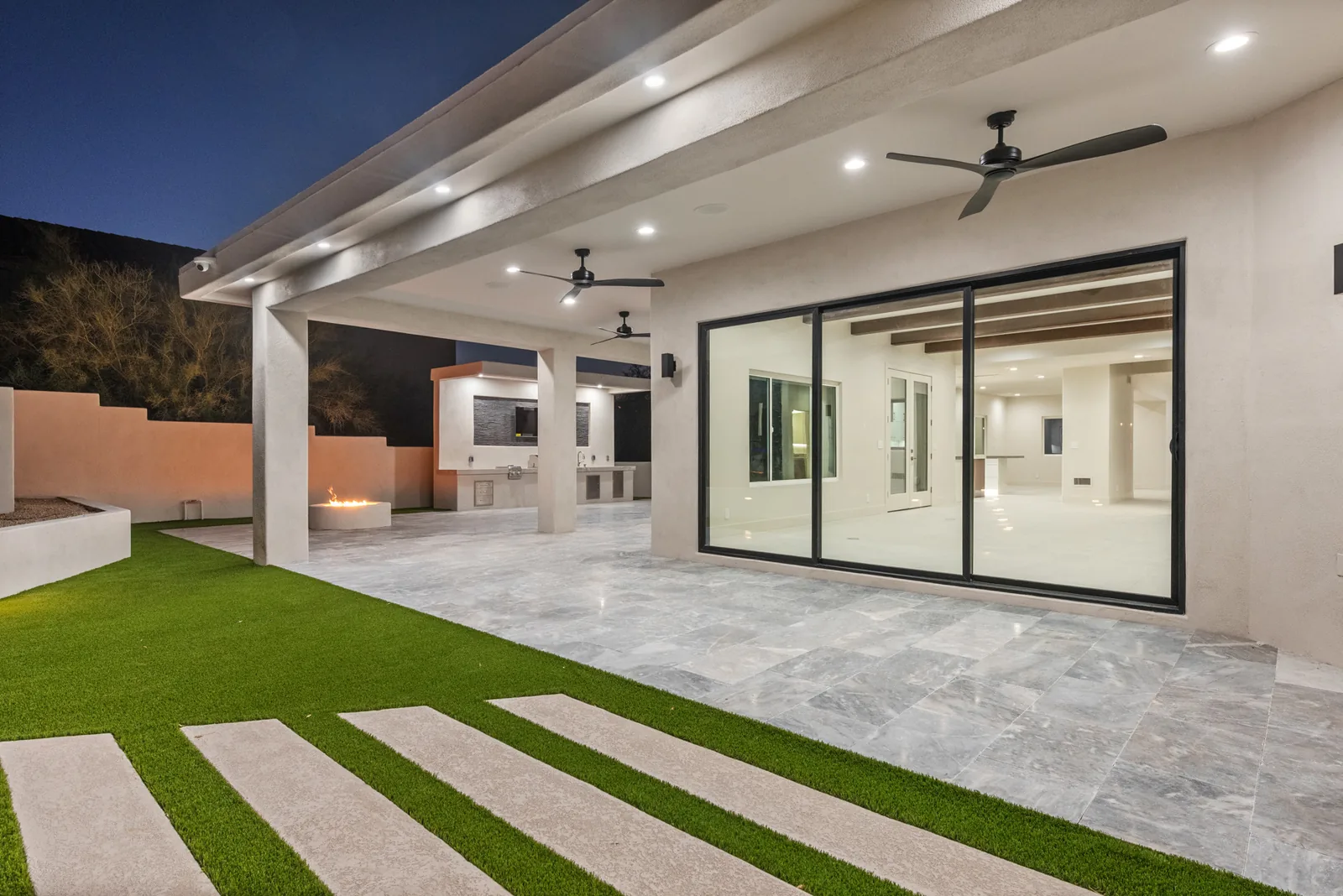 Dusk Patio & Turf: Full-width covered patio opening onto turf and paver banding, with sliding glass pockets to the great room.