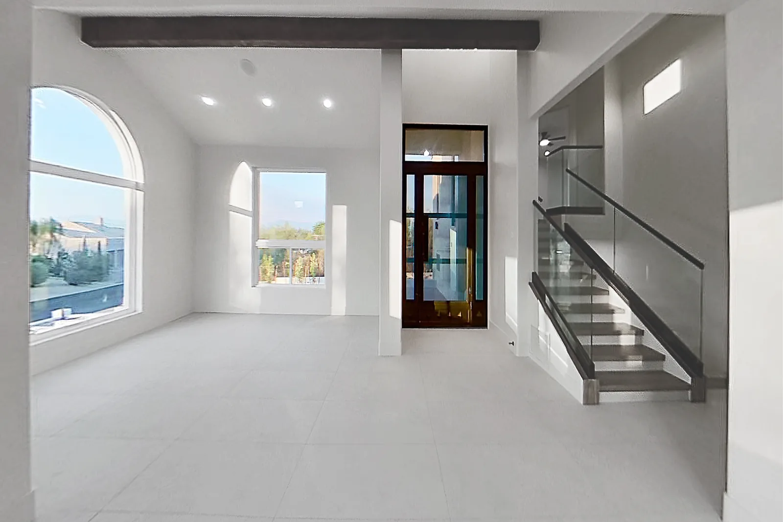 Entry Volume: Double-height entry with an arched window and an iron pivot door, stair beyond.
