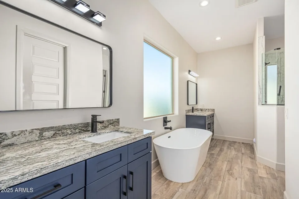 Freestanding Tub Suite: Primary bath with a freestanding soaking tub, navy vanity and a floor-mount filler, set by master plumbers in-house.